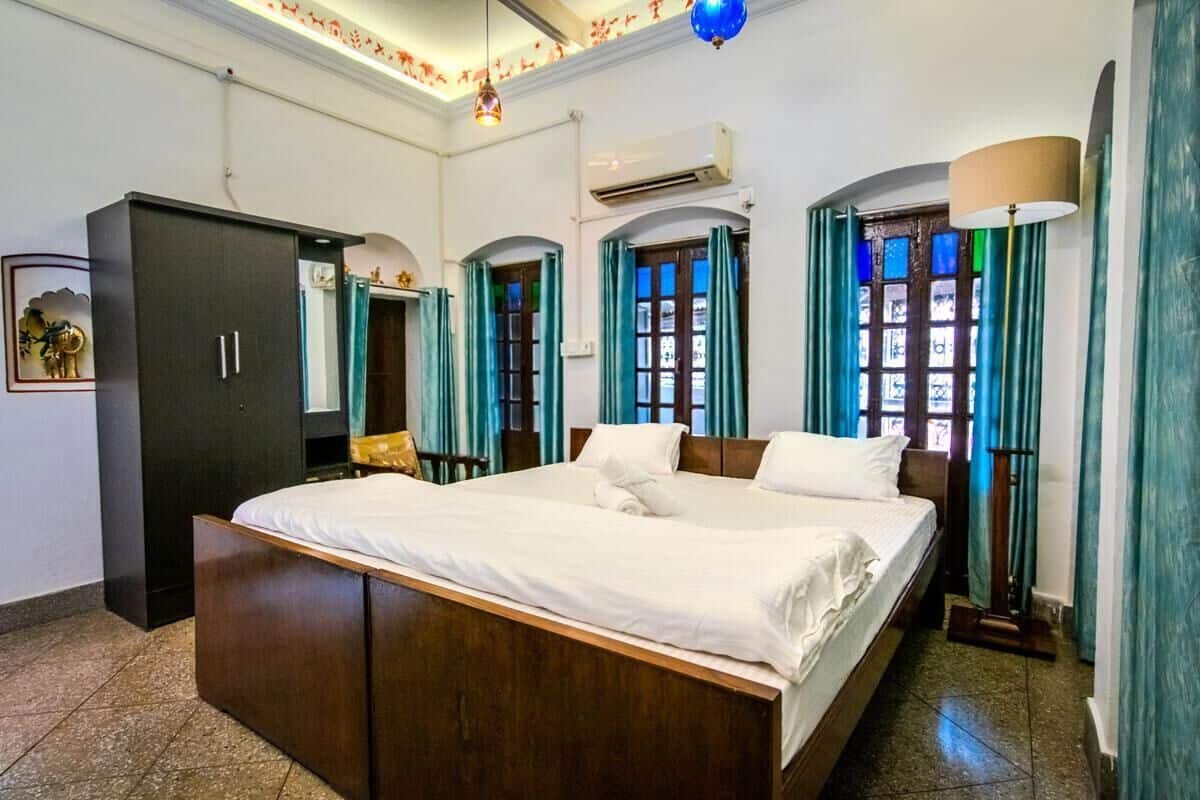 A hotel room with a large bed, wardrobe, and a window with curtains.