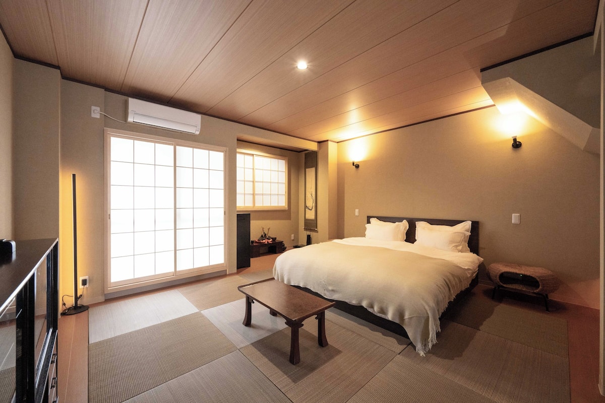 Un dormitorio con cama, mesita de noche, lámpara y un ventanal grande.