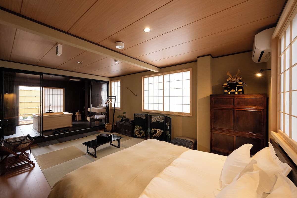 Un dormitorio de estilo japonés tradicional con suelo de tatami, una cama grande, puertas correderas y vistas al jardín.