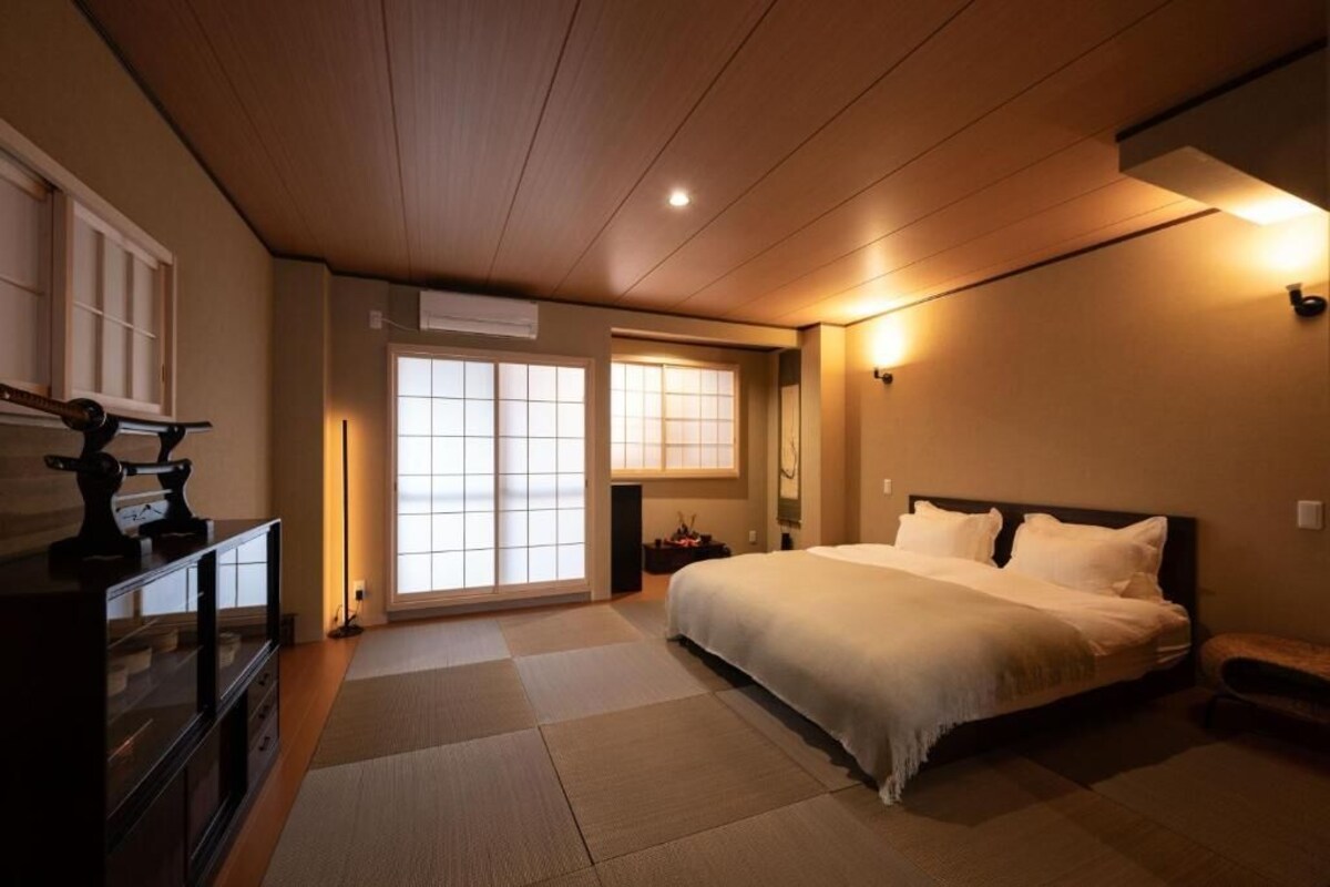 A bedroom with a bed, a dresser, a window with sliding doors, and a wall-mounted light fixture.