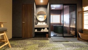 Une salle de bain moderne avec une porte en bois, un miroir rond, un lavabo avec des serviettes et une porte coulissante en verre donnant sur l’espace de la douche.