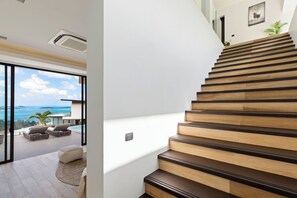 A modern staircase with wooden steps and a glass door leading to a balcony with a view of the sea. - Villa Sea Esta (Koh Samui)