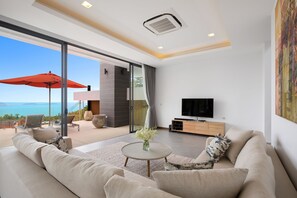 A modern living room with a sofa, coffee table, and TV, overlooking a balcony with a view of the sea. - Villa Sea Esta (Koh Samui)