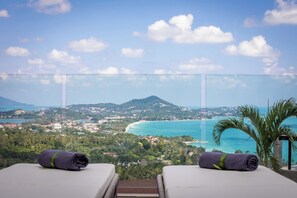A balcony with two sunbeds, a view of a coastal landscape, and a mountain in the distance. - Villa Sea Esta (Koh Samui)