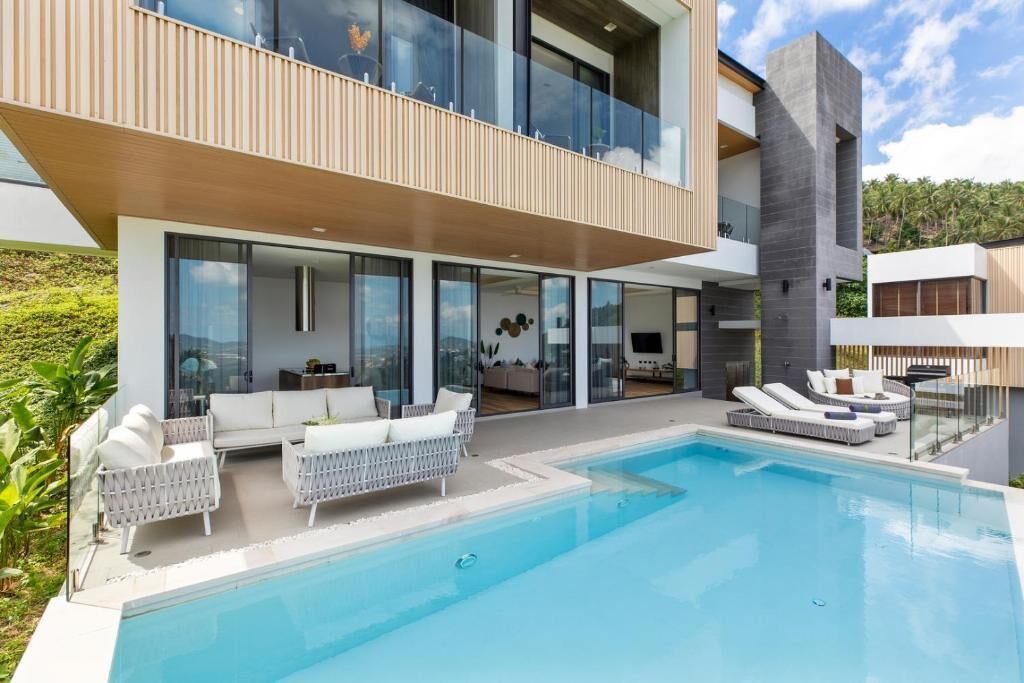 Una casa moderna de dos pisos con piscina, mobiliario exterior y ventanas amplias.