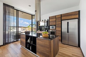 A modern kitchen with a central island, stainless steel appliances, and a view to the outside. - Villa Sea Esta (Koh Samui)