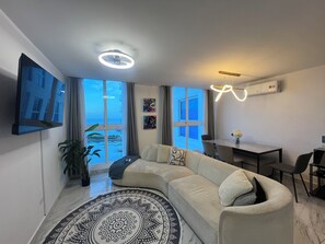 Ein modernes Wohnzimmer mit großem Fenster, einer Couch, einem Esstisch und einem Deckenventilator.