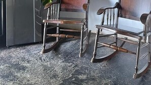 Un interior rústico con techo de lámina corrugada, vigas de madera, dos mecedoras, una planta en maceta y un armario de metal.