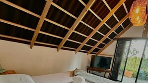 Habitación con techo alto, cama, televisor y vistas al exterior.