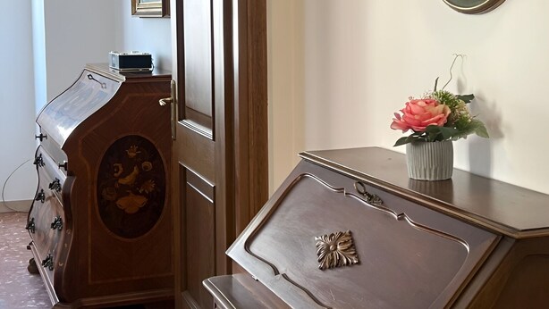 Una habitación con un aparador de madera, un espejo, un cuadro enmarco y un florero con flores.