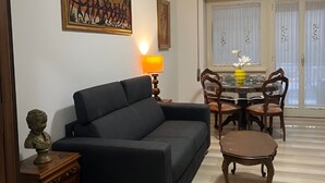 Una sala de estar con un sofá, una mesa de comedor con sillas, una lámpara y obras de arte en la pared.