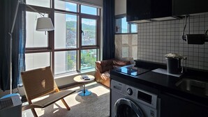 Une cuisine moderne équipée d’un lave-linge intégré, un coin repas avec une table et des chaises, et une grande fenêtre offrant une vue sur la ville.