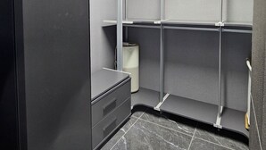 Une chambre moderne et minimaliste, dotée d’étagères intégrées, d’une armoire grise et d’un sol carrelé en marbre.
