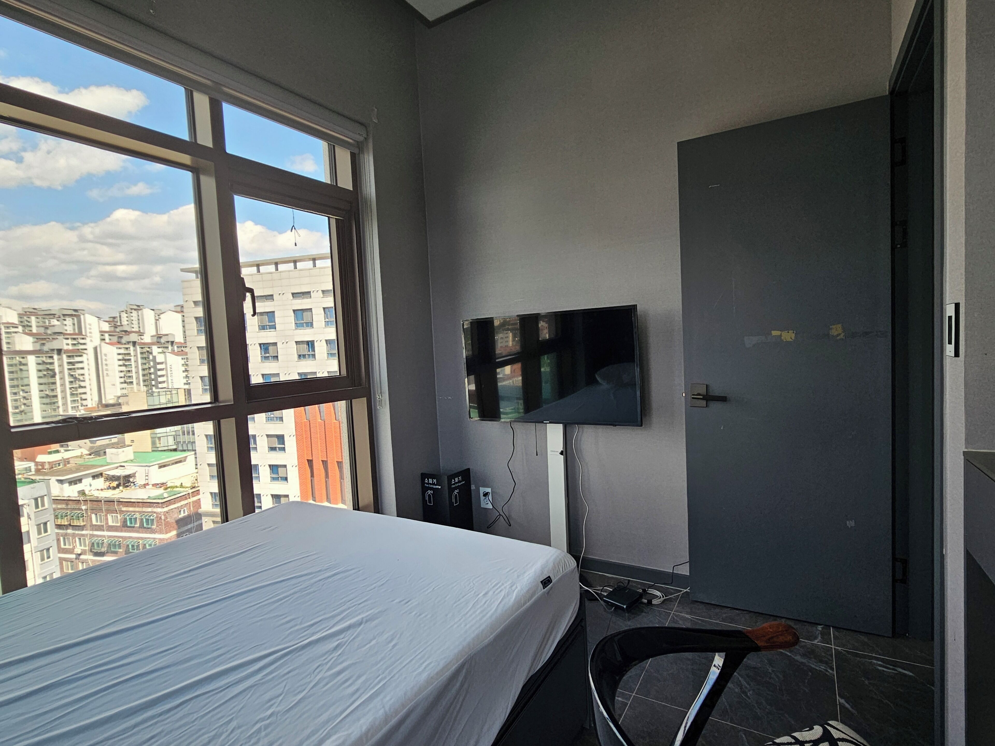 A hotel room with a bed, a TV mounted on the wall, a wardrobe, and a window offering a city view.