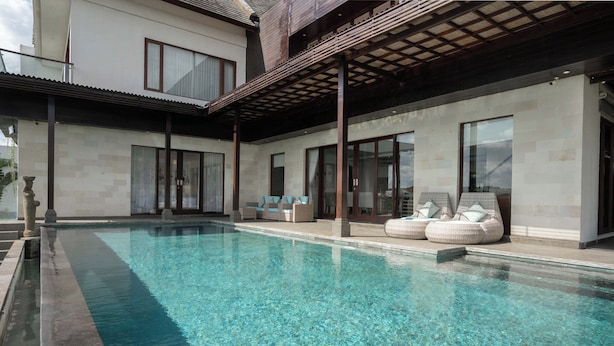 Et moderne poolområde med klart vand, en overdækket terrasse og siddepladser ved poolen.