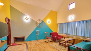 A living room with a wooden floor, a TV, a clock, a rocking chair, a sofa, and a window with curtains. - Emy Misty Charm Villa Ooty by VOYE HOMES (Ootacamund)