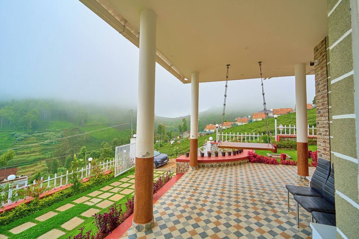 A covered terrace with a checkered floor, white pillars, and a view of a green valley.