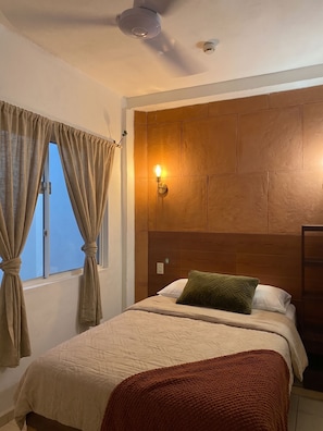 A bedroom with a bed, curtains, a wall-mounted light, and a ceiling fan.