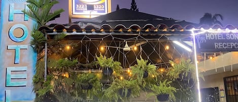 A hotel with a signboard, a reception area with plants, and a fence.