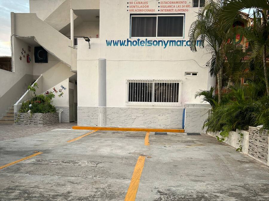 Entrada de hotel con un cartel, una escalera y un área de estacionamiento.