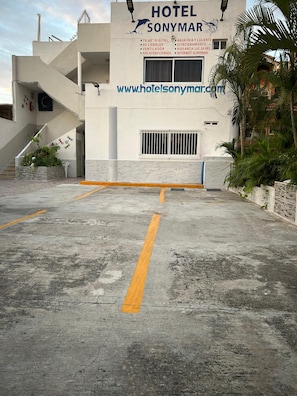 A hotel entrance with a sign, a staircase, and a parking area.