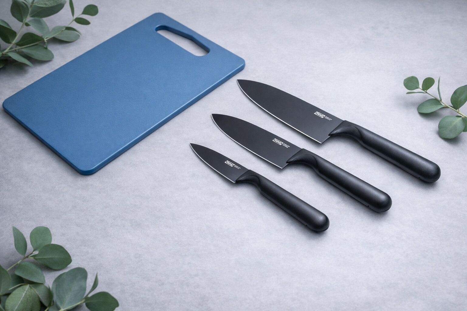 Tagliere blu con tre coltelli disposti su una superficie grigia.