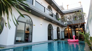 A modern building with a swimming pool, arched windows, and a pink flamingo float. - Song Bien Beach Villa Homestay (Hoa Hiep)