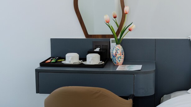 A hotel room with a desk, a chair, a bed, a mirror, and a vase with flowers. - Song Bien Beach Villa Homestay (Hoa Hiep)