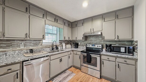 A kitchen with a granite countertop, stainless steel appliances, and light gray cabinetry.