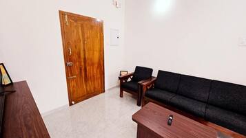 Una habitación con puerta de madera, un sofá negro, una mesa de madera y un cuadro en un escritorio.