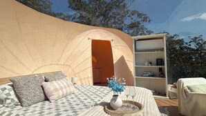 A tented accommodation with a bed, pillows, a tray with flowers, and a bookshelf.