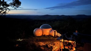 A spherical structure with a dome and a cylindrical section, surrounded by trees and a view of distant hills.