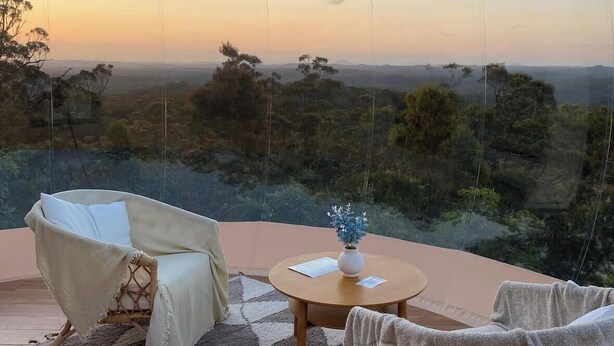 A room with a view of a landscape, a round wooden table, and two wicker chairs.