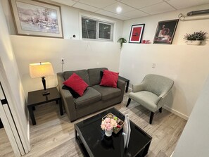 Una sala de estar con sofá, sillón, mesa de centro, lámpara y cuadros en la pared.