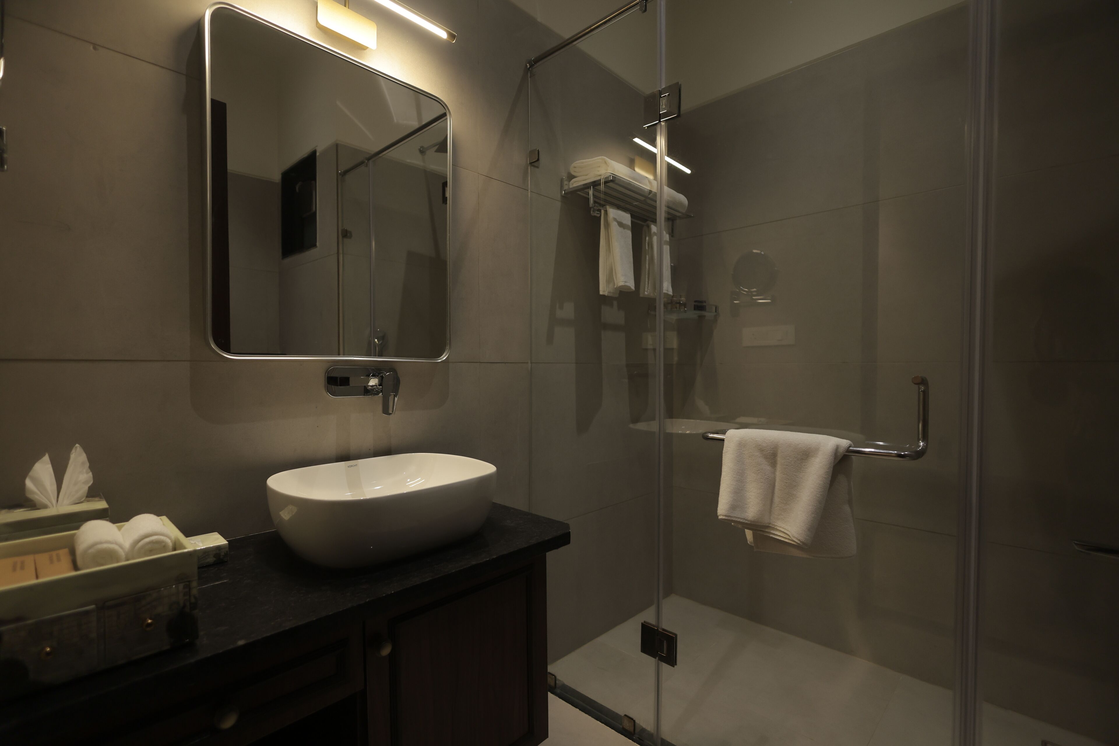 Un baño moderno con un espejo grande, un lavabo y zona de ducha con mampara de vidrio.