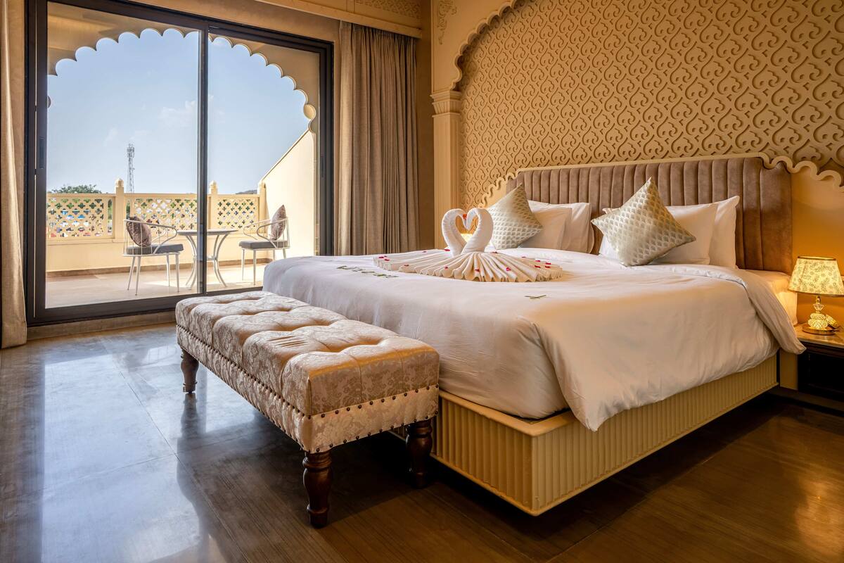 Un dormitorio amplio con una cama grande, un banco y vistas a través de un ventanal.