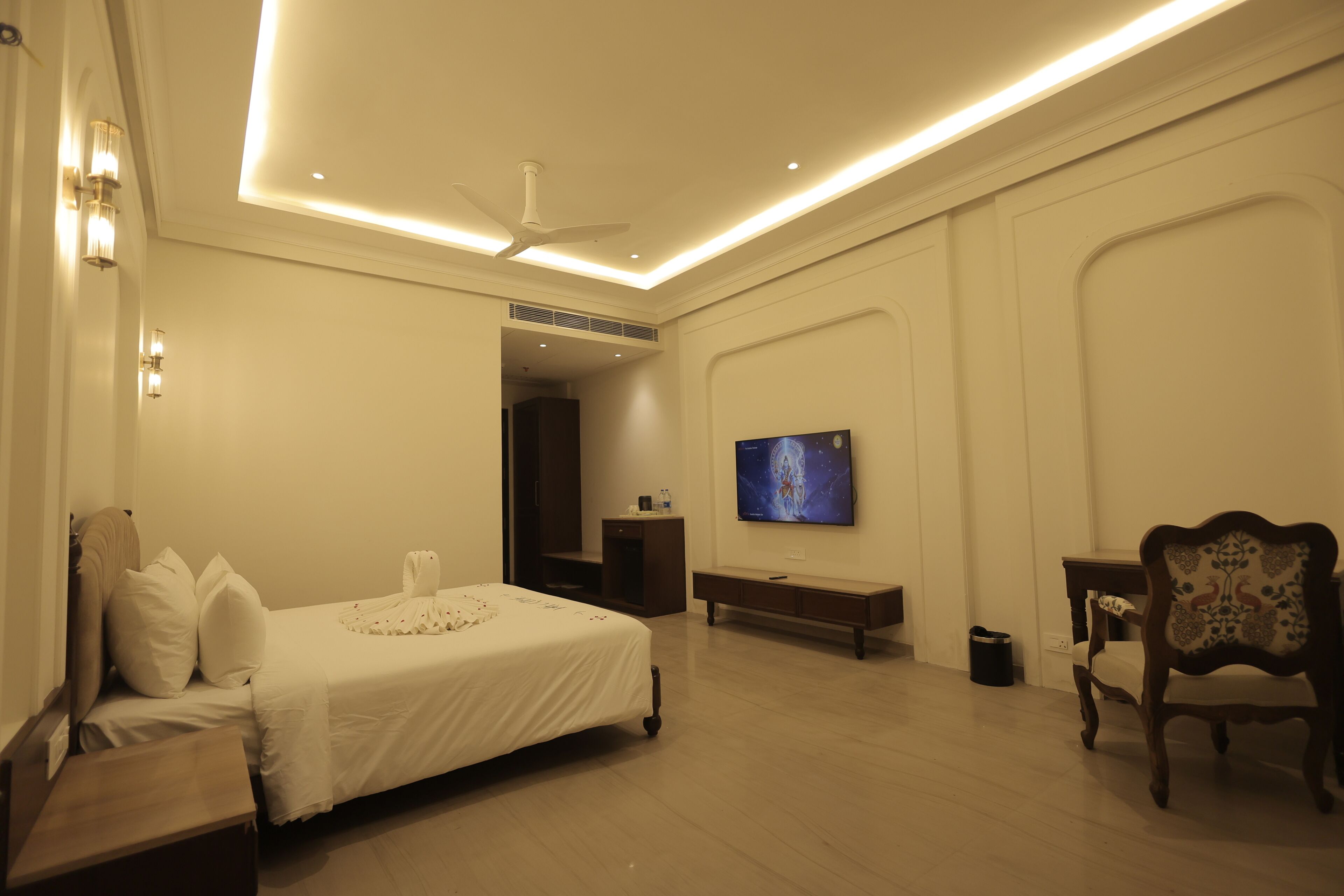 A bedroom with a bed, a television, a ceiling fan, and a desk.