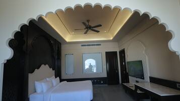 Una habitación de hotel con cama, ventilador de techo, televisor y vistas al exterior.
