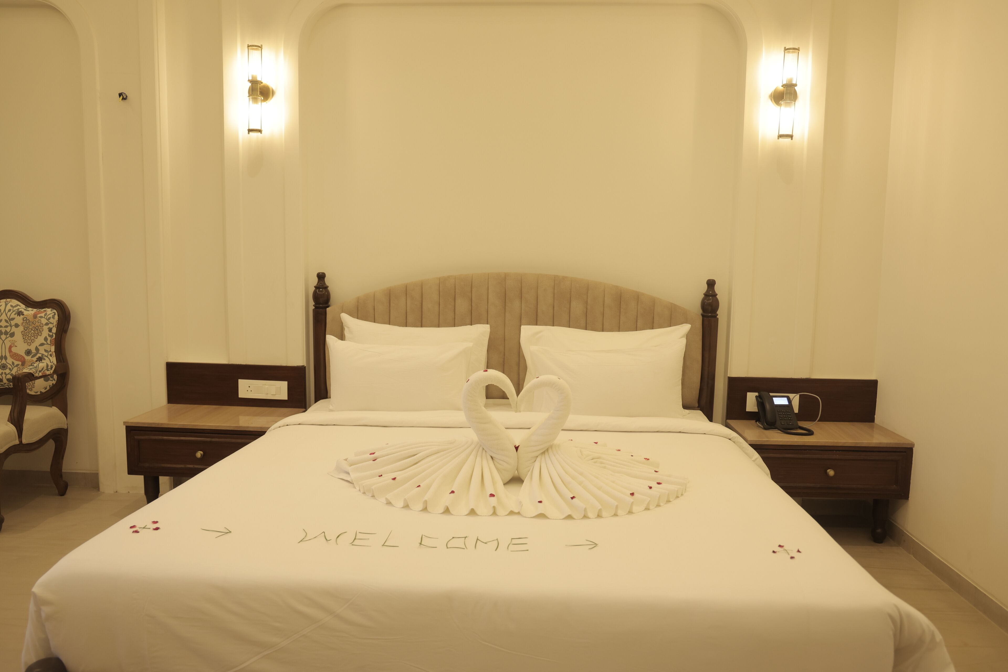 Une chambre d’hôtel avec un grand lit, deux tables de chevet, une chaise et un luminaire fixé au mur.