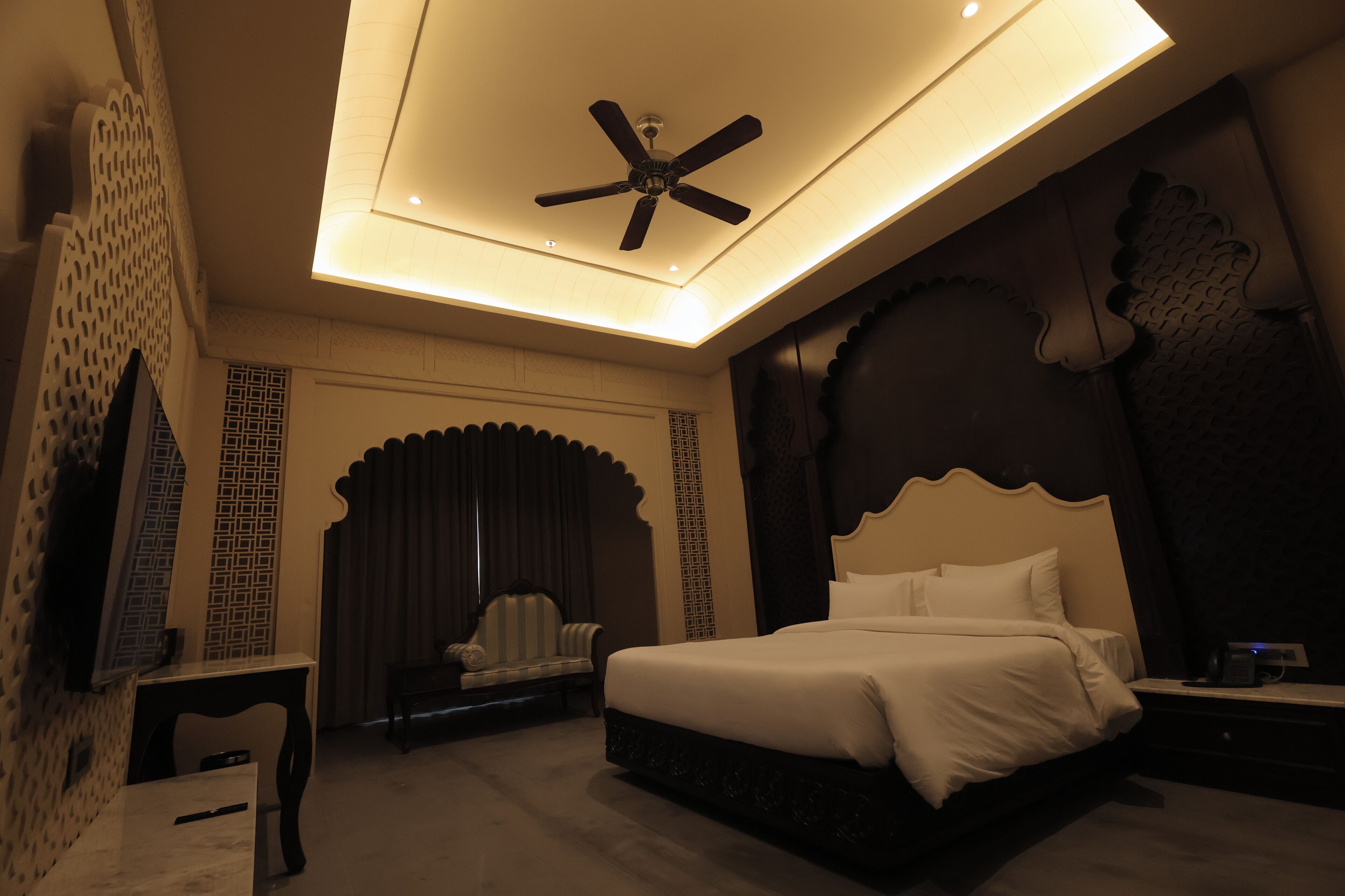 A bedroom with a bed, a desk, a chair, a ceiling fan, and decorative wall panels.