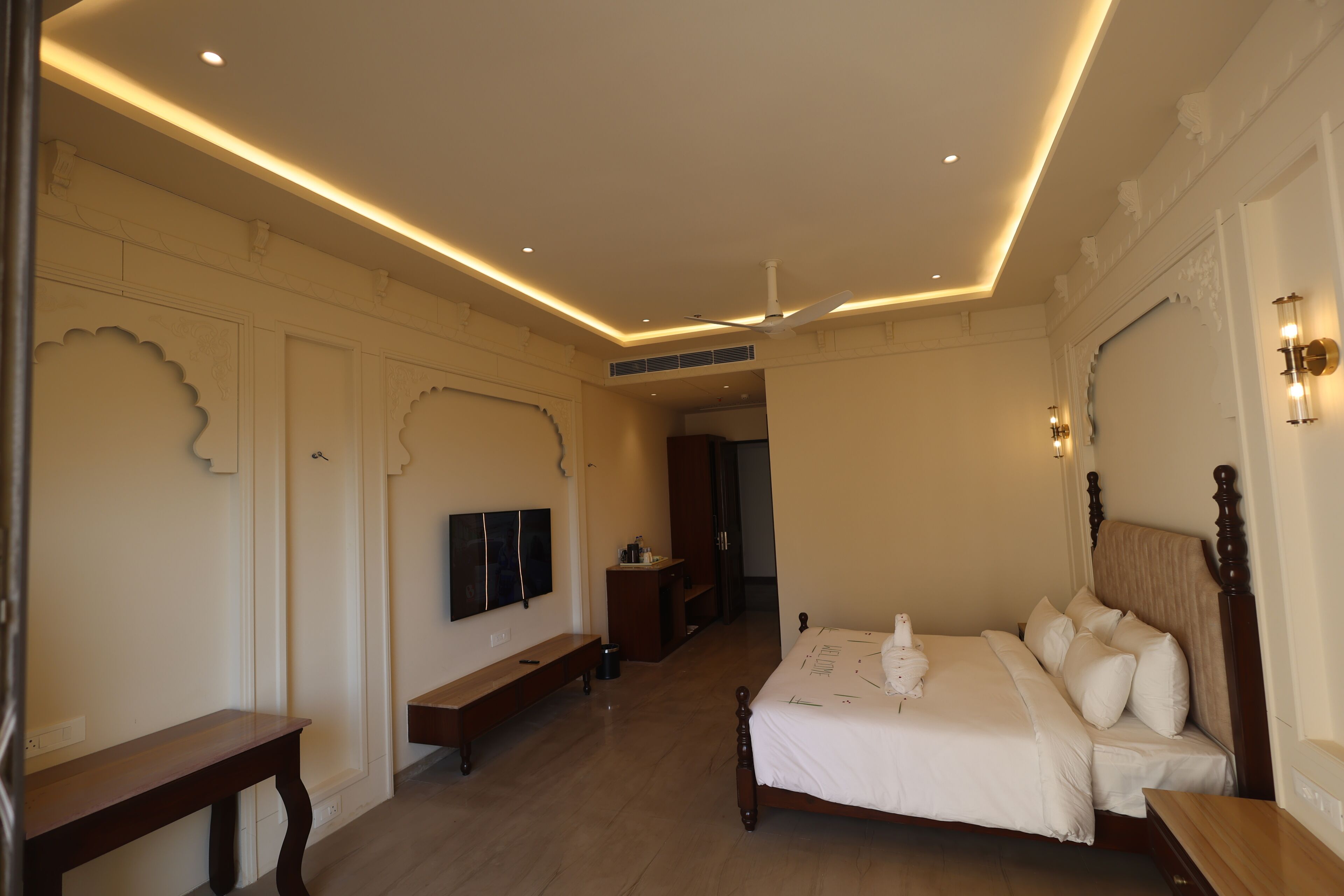 Ein Schlafzimmer mit Bett, einer Bank, einem Fernseher und einem Deckenventilator.