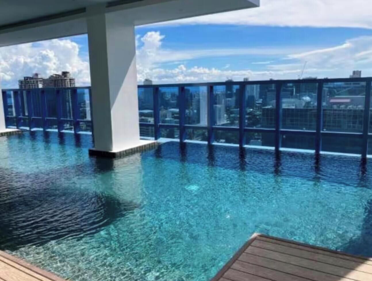 Una piscina infinita en la azotea con agua azul cristalina, rodeada por una barandilla de cristal y un horizonte urbano de fondo.