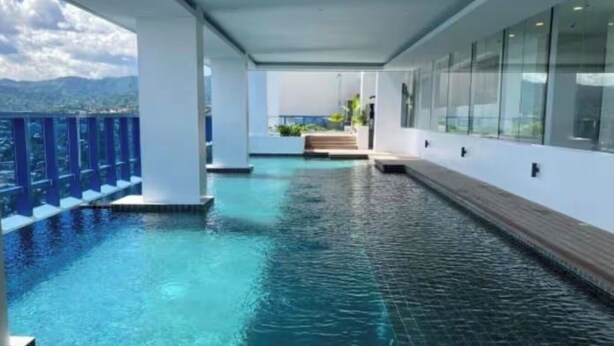 A pool area with clear water, a wooden deck, and a view of mountains. - Luxury Studio 38 Park Ave (Cebu City)