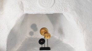 A white textured wall with a recessed area containing a small black stand and two golden decorative objects. - Artemis cottage Mykonos (Mikonos)