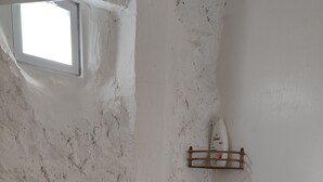Een badkamer met een witte, geribbelde wand, een klein raam, een douche met een messing kraan en een zeepdispenser op een plank.
