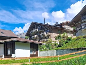 A residential building with multiple balconies, a sloped roof, and a view of mountains in the background. - Sans Souci O2 by Interhome (Grindelwald)