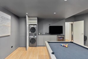 A modern room with a pool table, a washing machine, a TV, and a large painting on the wall. - Terrigal Apartment: Panoramic Ocean Views, Hot Tub (Terrigal)