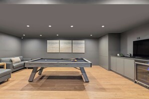 A modern living room with a pool table, a sofa, a flat-screen TV, and a kitchen area. - Terrigal Apartment: Panoramic Ocean Views, Hot Tub (Terrigal)