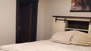 Quarto com cama, cabeceira, porta e quadro fixado na parede.