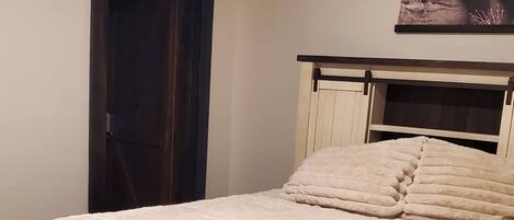 A bedroom with a bed, a headboard, a door, and a wall-mounted picture.